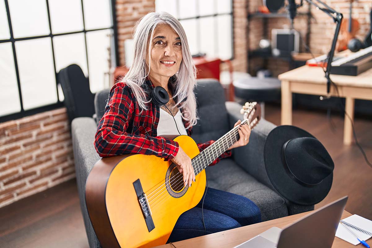 Woman wearing headphones aorund her neck while holding a guitar