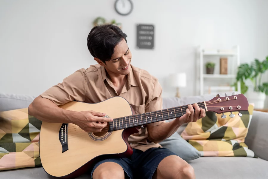 Young man practicing acoustic guitar on the couch in the living room